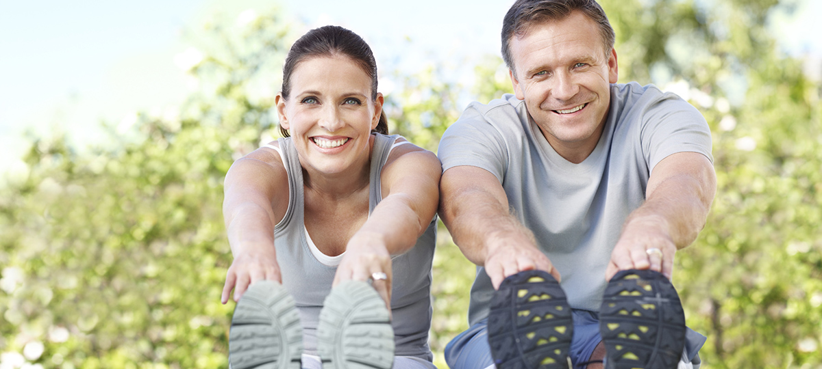 Smiling mature couple wearing sportswear while sitting outdoors in a park and stretching